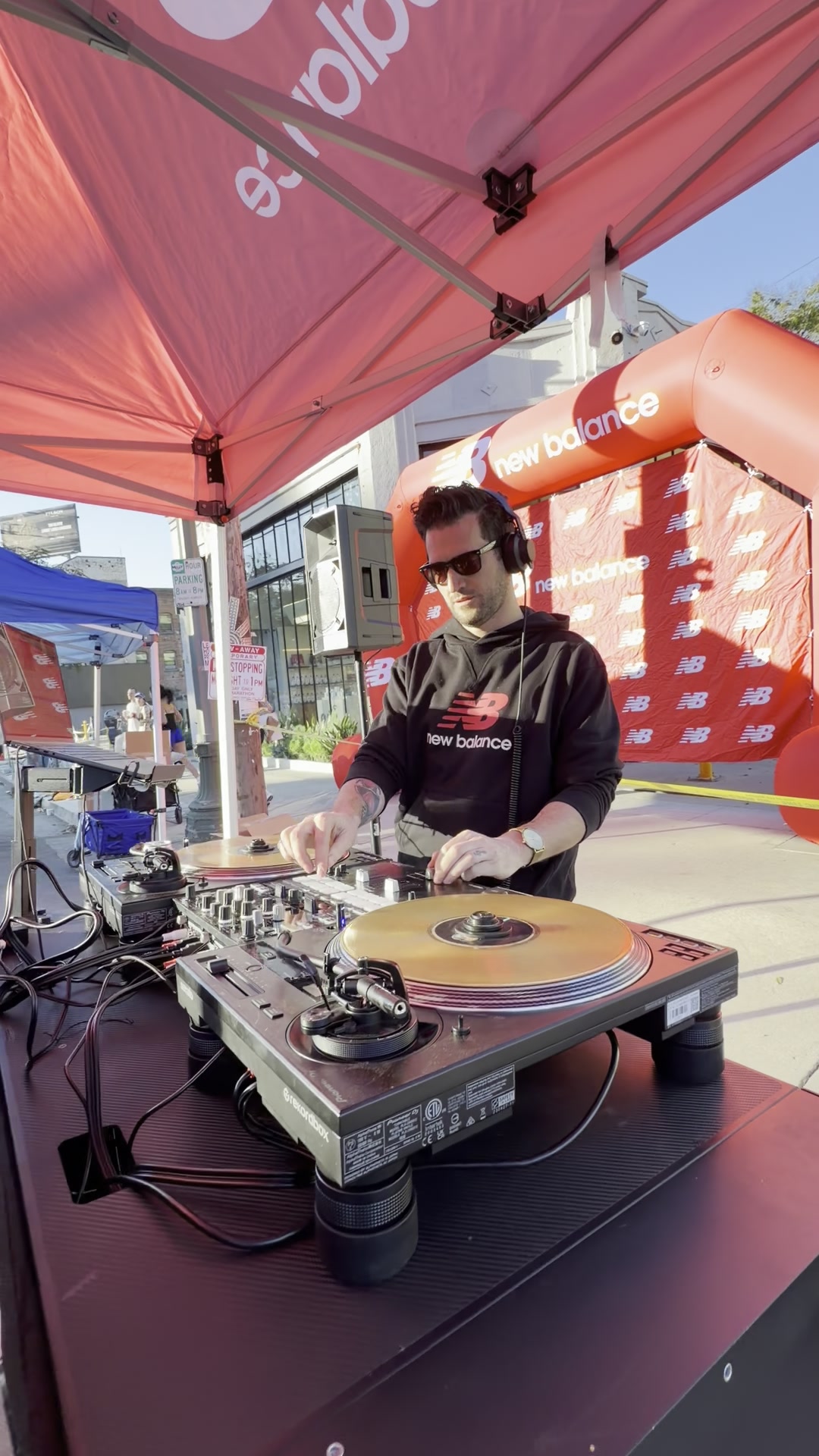 Miles mixing on turntables under a branded tent on a closed street, with an inflatable race arch behind him.