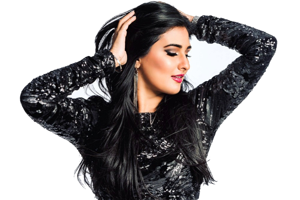 DJ Miss Ninja in a black sequined top, eyes closed, both hands lifted into her hair against a white studio backdrop.