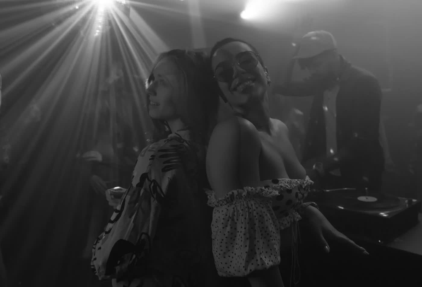 Two guests dancing back to back in black and white, the DJ working behind them.