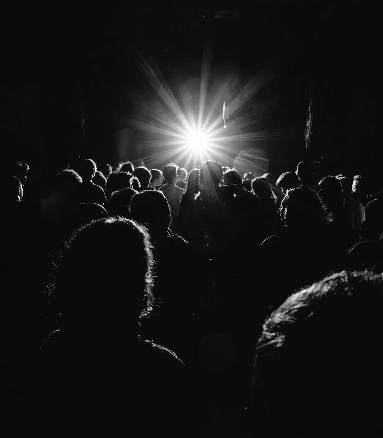 A black-and-white crowd in silhouette, backlit by one hard light.